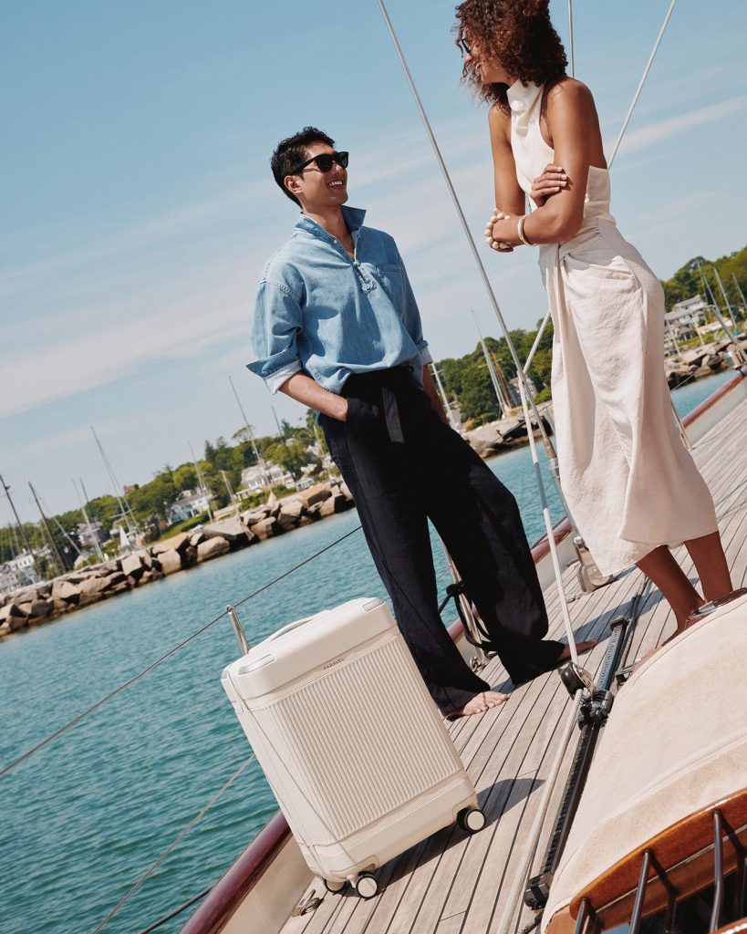 Paravel Aviator Carry-On in Nantucket Cream on the teak deck of a sailboat in a New England harbor