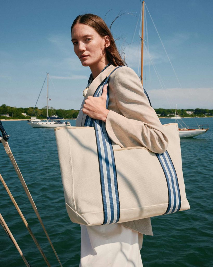 Signature Canvas Tote, Nantucket Cream Paravel Signature Canvas Tote in Nantucket Cream with blue striped webbing handles, carried on a sailboat